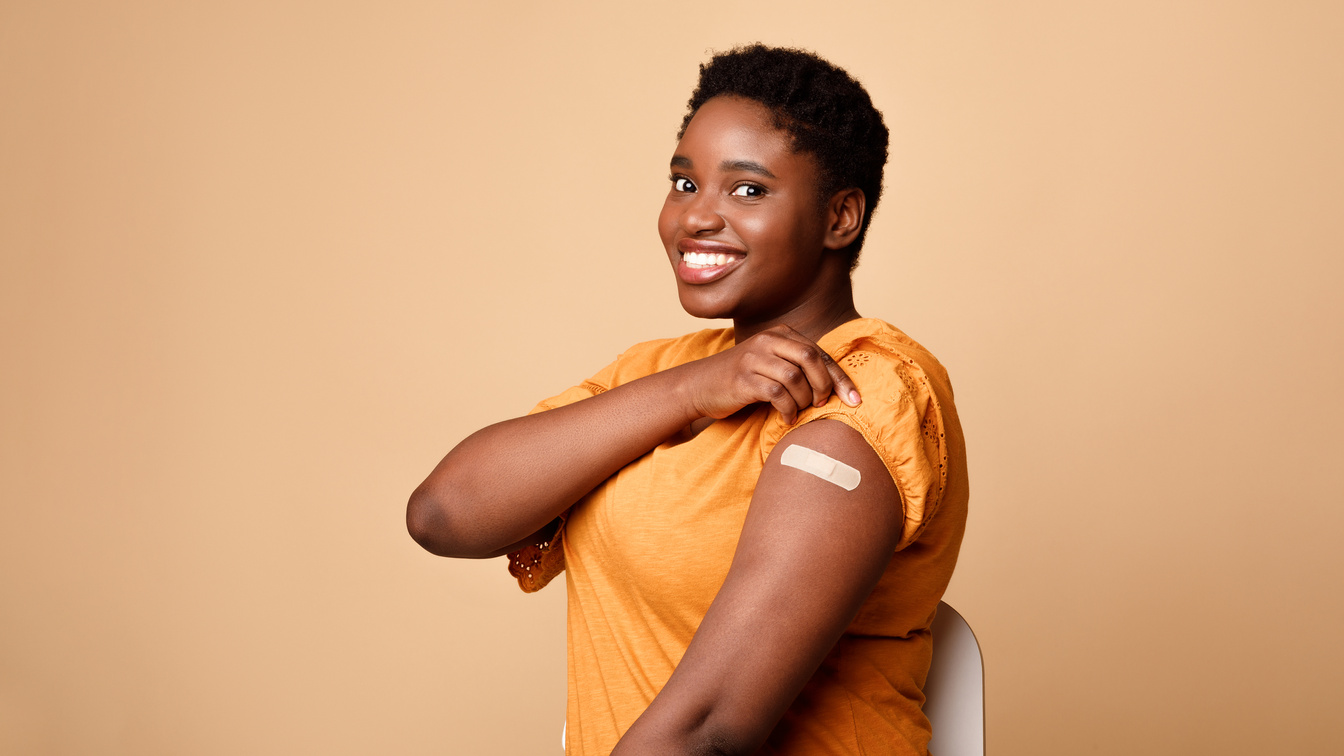 Black Woman Showing Vaccinated Arm After Vaccine Injection, Beige Background